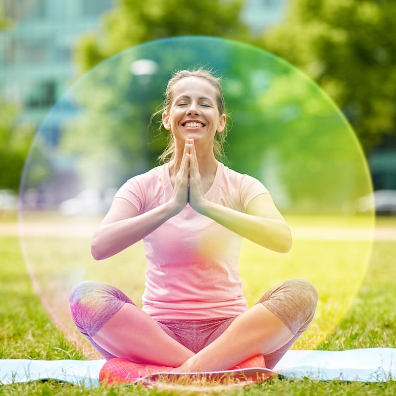 fitness, yoga and healthy lifestyle concept - happy woman meditating in summer park over rainbow aura